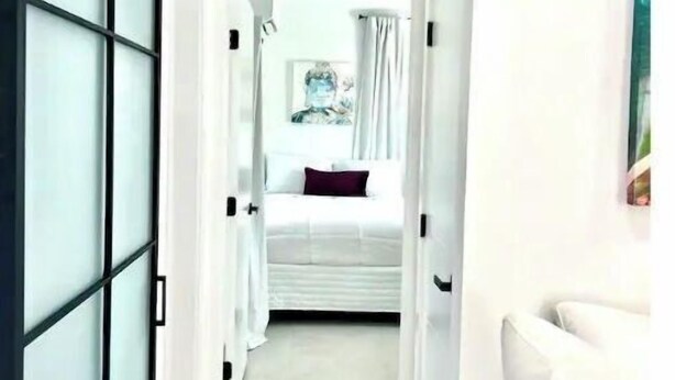 Ein Flur, der zu einem Schlafzimmer führt, mit einem Bett, einem weißen Sofa und einem Bild an der Wand.