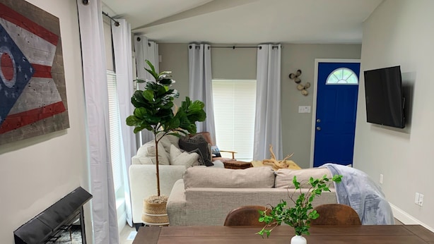 A modern living room with a fireplace, a dining table with four chairs, a ceiling fan, and a blue door. - Perfect for Fall Getaway - Firepit : Walk to Water (Buckeye Lake)