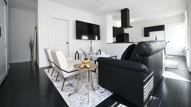 A modern living room with a black sofa, white armchair, and a coffee table with a decorative centerpiece. - 191 Seymour, Ave. Derby · Spacious Renovated 3 bedroom near GriffinHospital (Derby)