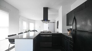 A modern kitchen with a central island, black cabinetry, and a stainless steel refrigerator. - 191 Seymour, Ave. Derby · Spacious Renovated 3 bedroom near GriffinHospital (Derby)