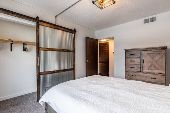 A bedroom with a bed, a wooden wardrobe, a sliding barn-style door, and a ceiling light fixture.