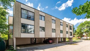 A modern multi-story building with a flat roof, large windows, and a parking area with a car. - Comfy 1 bed/1 bath - 6 blocks from Mayo (Rochester)