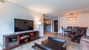 A modern living room with a flat-screen TV, wooden entertainment unit, a coffee table, a leather recliner, and a dining area with a table and chairs. - Modern, Rustic 2 Bed/1 bath 6 blocks from Mayo (Rochester)