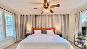 Ein Schlafzimmer mit einem großen Bett, einem Deckenventilator, Vorhängen, einem Nachttisch und einem Bücherregal.
