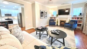 Ein Wohnzimmer mit einer Couch, zwei Couchtischen, einem Kamin, einem Fernseher und einer Küche im Hintergrund.