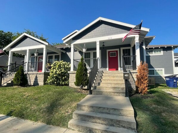 A residential building with a red door, a covered front porch, and a flag.