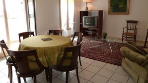 A dining area with a round table and chairs, a television set on a stand, a sofa, and a painting on the wall. - Le Vieux Saint Vincent (MACON)