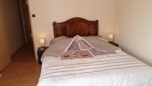 A neatly made bed with a patterned bedspread, two bedside lamps, and a wooden headboard. - Le Vieux Saint Vincent (MACON)