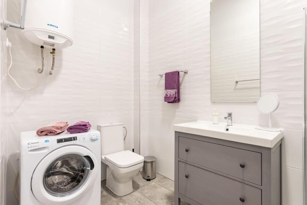 A modern bathroom with a washing machine, toilet, vanity, and a mirror.