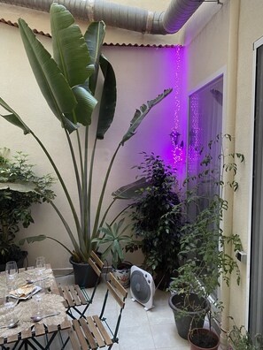Un espace patio avec une table dressée pour les repas, entouré de différentes plantes en pot et agrémenté d’un ventilateur.