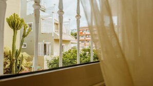 Blick aus dem Fenster auf ein Gebäude mit Balkonen, einem Kaktus und etwas Grün.