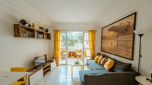 Ein Wohnzimmer mit Fernseher, einer Couch und einem Essbereich mit gelben Stühlen.