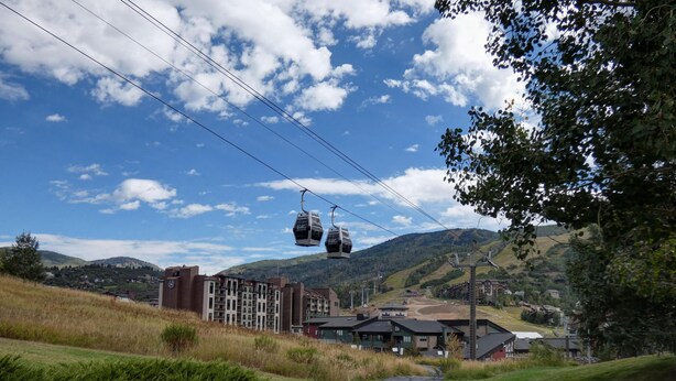 A ski lift with cabins, a paved path, buildings, and a mountainous backdrop. - New Listing -- Modern on the Mtn -- Steps to Ski! (Steamboat Springs)