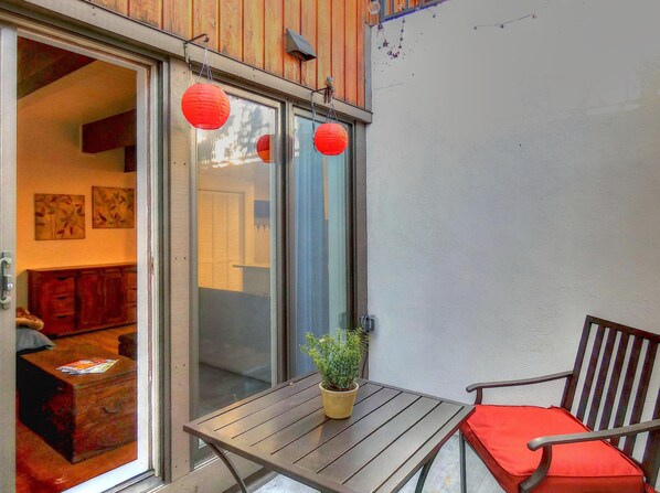 A wooden table with a potted plant and a red cushion, a sliding glass door, and a red lantern hanging above.