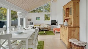 Un salon moderne avec un coin repas, de grandes fenêtres et un meuble en bois.