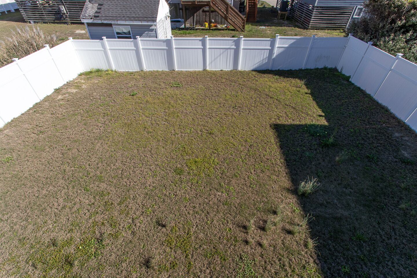A fenced backyard with a grassy area and a wooden deck.