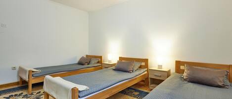 Une chambre avec trois lits simples, chacun doté d’une tête de lit en bois et d’une table de chevet avec une lampe. La chambre est dotée d’un sol recouvert de moquette à motifs floraux.