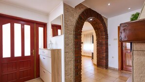 A hallway with a red door, a white cabinet, a brick archway, and a tiled floor. - Stunning home in Gudovac (Gudovac)