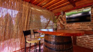 A rustic bar area with a wooden barrel, two chairs, a TV mounted on a brick wall, and a decorative wall with vertical elements. - Stunning home in Gudovac (Gudovac)