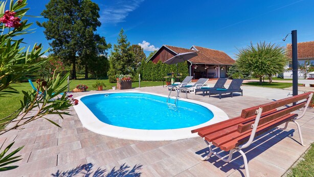 A swimming pool with lounge chairs and a wooden bench, surrounded by a patio area with a small building and trees. - Stunning home in Gudovac (Gudovac)