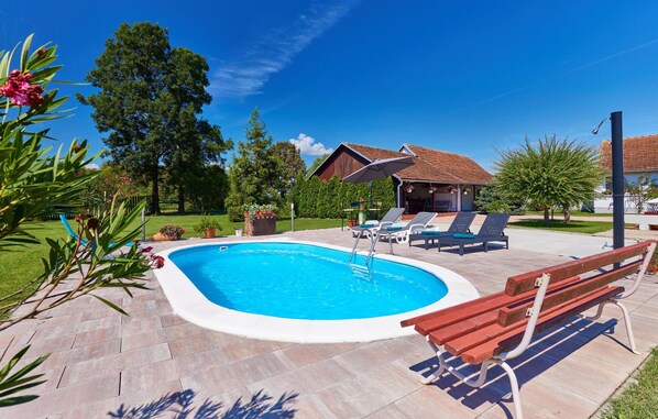 Relax by the pool surrounded by lush greenery and trees, with lounge chairs and a bench for unwinding.