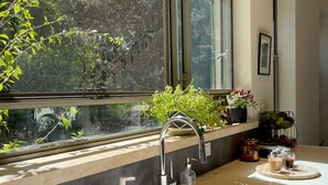 Una cocina moderna con un ventanal grande, un lavamanos de acero inoxidable y una encimera con una tabla de cortar y dos vasos de té helado.