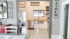 A dining area with a table and chairs, a kitchen with a window and cabinets, and a sign that says "GATHER here".