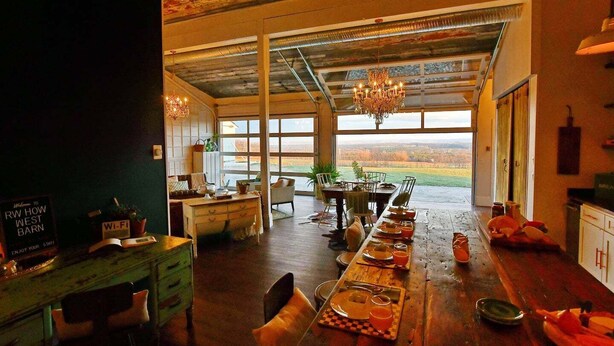 A spacious dining area with a long table set for a meal, a chandelier, and a view of the outdoors. - Sleep in a barn while enjoying the luxury accommodations  and friendly farm animals on property! (Perry)