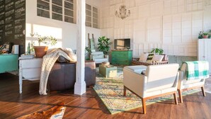 A spacious living room with a high ceiling, wooden flooring, and a mix of modern and vintage furniture. - Sleep in a barn while enjoying the luxury accommodations  and friendly farm animals on property! (Perry)