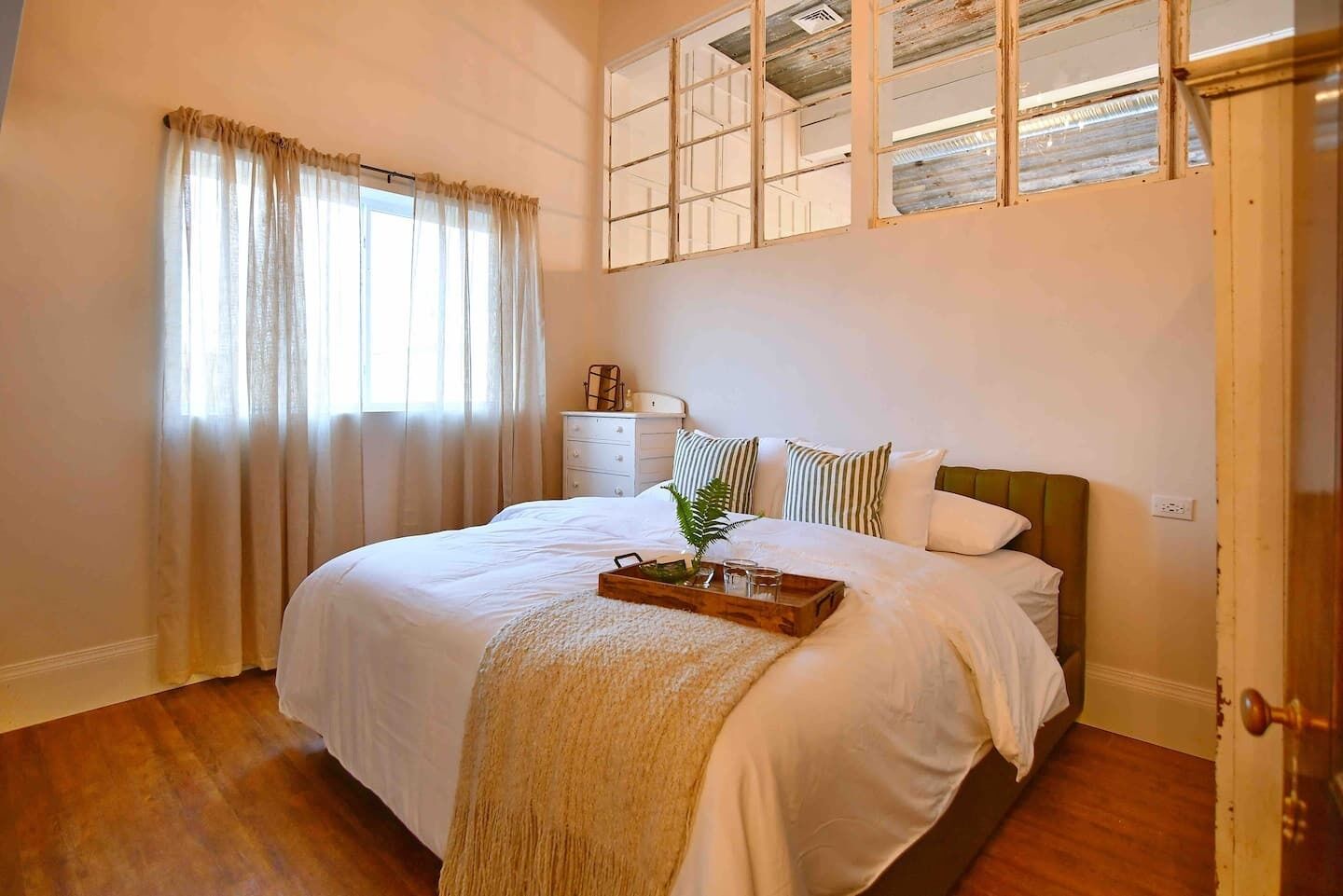 Un dormitorio con una cama grande, una mesita de noche de madera, una ventana con cortinas y vistas al cielo.
