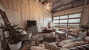 A spacious living room with a large window, a chandelier, and a television. - Sleep in a barn while enjoying the luxury accommodations  and friendly farm animals on property! (Perry)