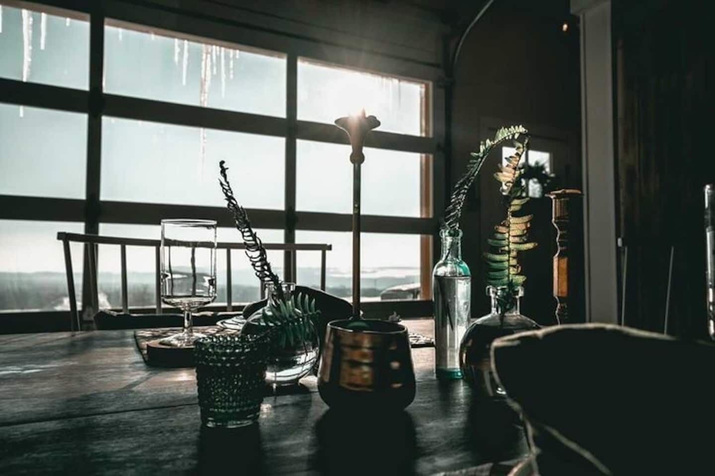 A room with a large window, a wooden table, and various decorative items including a glass bottle, a metal sculpture, and a potted plant.