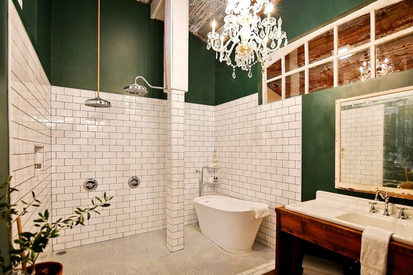 Un baño con azulejos blancos tipo metro, una bañera independiente, un tocador de madera y una araña.