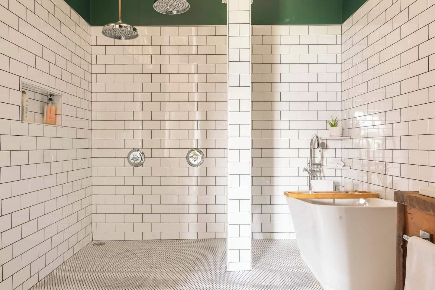 Un baño moderno con azulejos blancos tipo metro, ducha con puerta de cristal, bañera independiente y un estante pequeño con artículos de aseo.