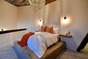 A bedroom with a bed, a nightstand, a wall-mounted shelf, and a staircase. - Southview @ the West Barn - Great Letchworth View! (Perry)