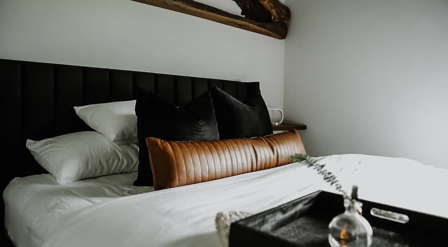 Un lit bien fait, avec du linge de lit blanc et une tête de lit en cuir marron.