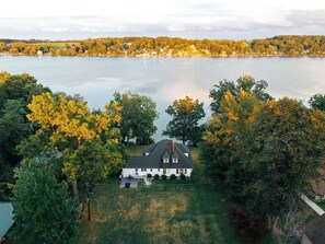 An aerial view of a house with a lawn and trees, overlooking a body of water.
