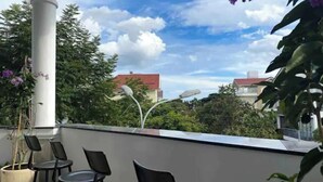 A balcony with four black chairs, a white column, and a view of houses and trees under a partly cloudy sky.