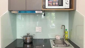 A compact kitchen with a microwave, a pot on an induction cooktop, a sink, and a bottle of dish soap.