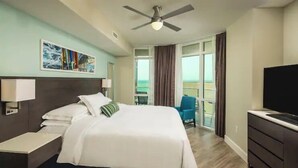 Une chambre d’hôtel équipée d’un lit, d’une télévision, d’un bureau, d’une chaise et d’un balcon avec des rideaux.