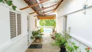A narrow corridor with a stone floor, white walls, and a wooden ceiling structure. There are potted plants and a chair along the corridor. - Nice & Cosy Apartm. for max. 4 Guests next to Pool (Sosua)