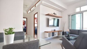 Ein modernes Wohnzimmer mit Glastisch, grauem Sofa und einem an der Wand befestigten Flachbildfernseher.