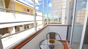 Ein Balkon mit Glastisch und Stuhl, einem weißen Geländer und Blick auf die Stadt.