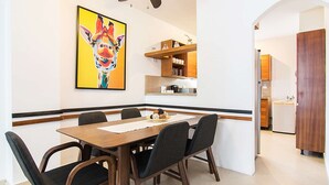A dining area with a wooden table and chairs, a painting of a giraffe, and a kitchen in the background.