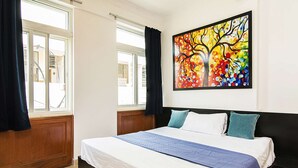 A bedroom with a large bed, a window with curtains, and a colorful painting on the wall.