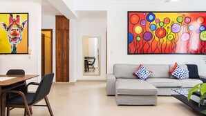 A modern living room with a sofa, a dining table with chairs, and a large abstract painting on the wall.