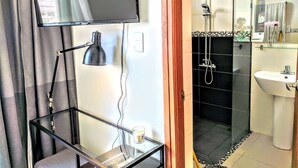 Un baño moderno con cabina de ducha de vidrio, un televisor montado en la pared y una mesita de noche con una lámpara y una vela.