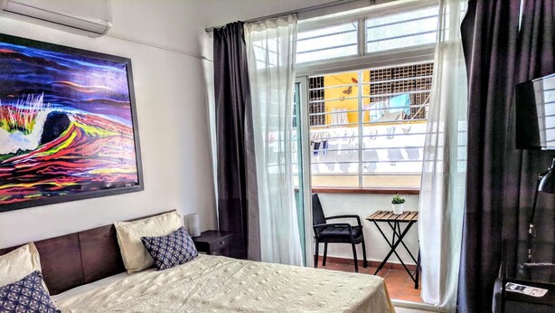 Habitación de hotel con una cama grande, un cuadro en la pared, un balcón con mesa y silla, y vistas al exterior.