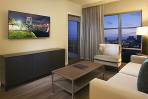 A hotel room with a large window offering a city view, a flat-screen TV mounted on the wall, a dark-colored console table, and a beige armchair. - Orlando | Lakeside Escape | Resort Pool & Theme Parks Nearby (Orlando)