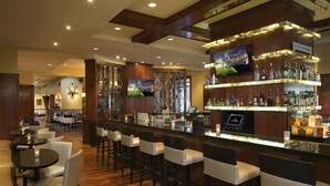 A bar area with a long counter, multiple stools, and a television screen.